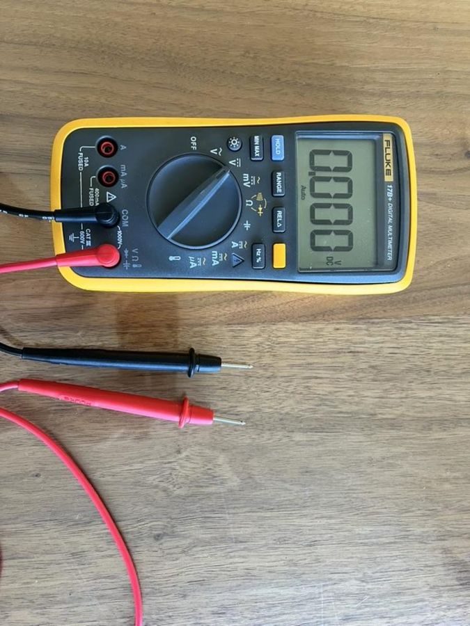 A digital multimeter with red and black probes on a wooden table