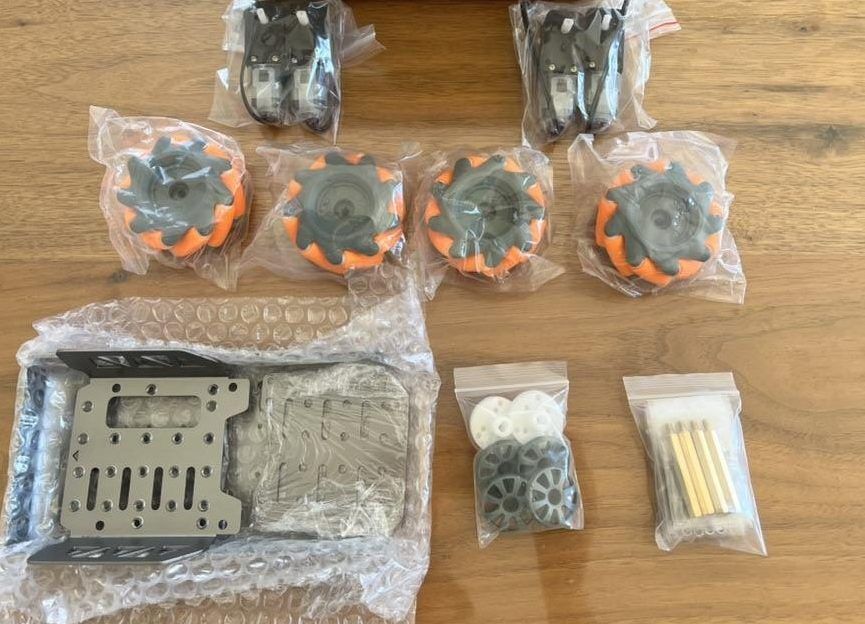 Robot parts in their packaging: mecanum wheels, motors, a metal chassis, and hardware
