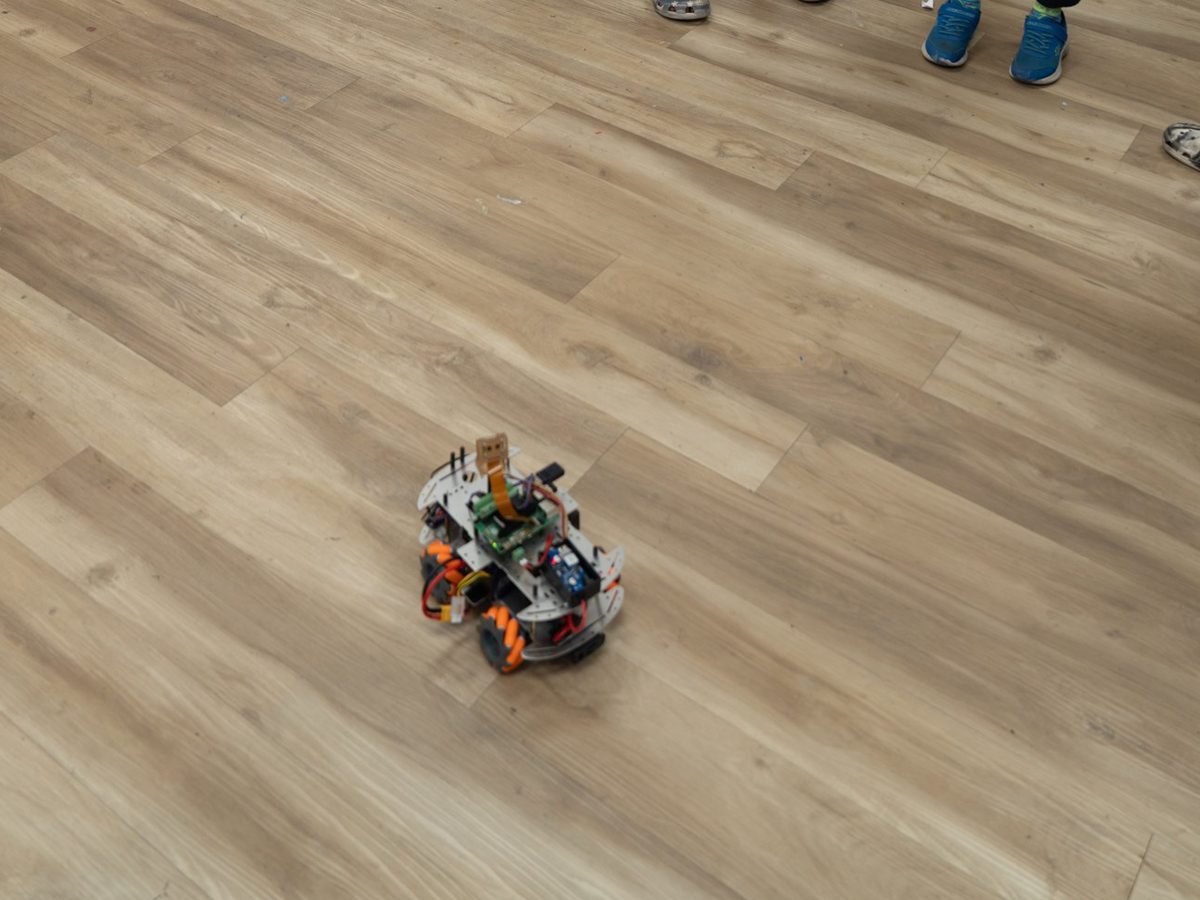 A small mobile robot with a camera moving across the floor, steered by a student with a game controller