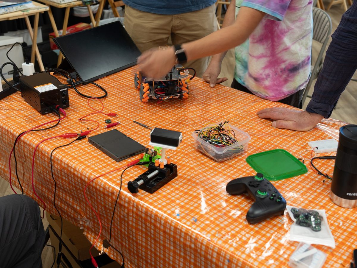 A workbench with a mobile robot, a power supply, a multimeter, wires, and a game controller